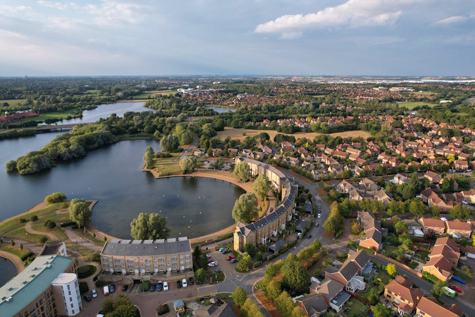 Aerial black-and-white photograph of Southmere Lake estate in Thamesmead showing the lake with its curved shoreline and small islands surrounded by landscaped gardens and residential buildings. The im
